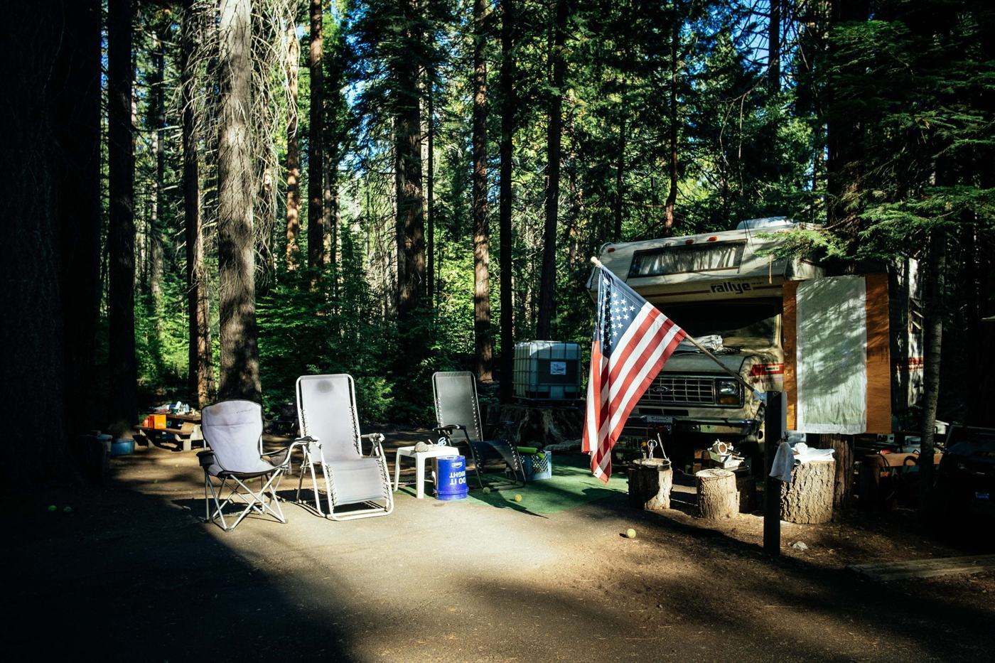 Campsite with a trailer and folding chairs under tall trees